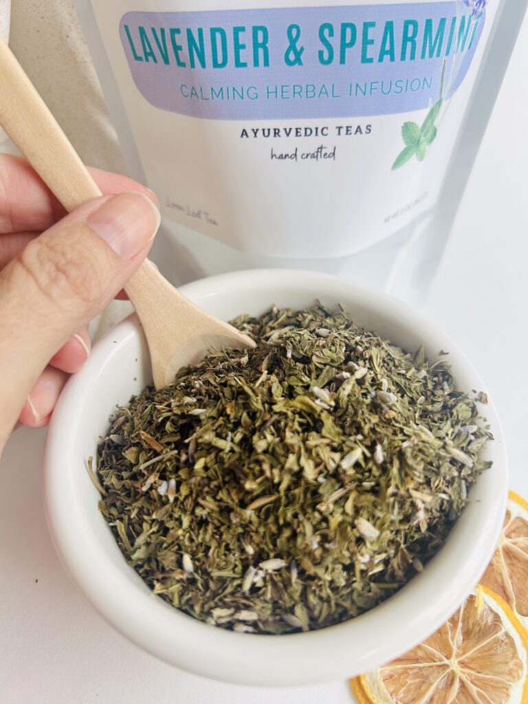 lavender spearmint herbal tea displayed in a minimalist setting with a white mug and soft neutral tones, organic caffeine free herbal tea with visible lavender buds and spearmint leaves, calming floral mint blend designed for daily wellness rituals and mindful living, cozy tea aesthetic, herbal tea for relaxation and balance, wellness tea gift idea, tea presentation for self care and peaceful lifestyle