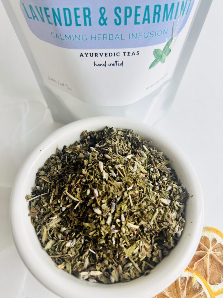 lavender spearmint herbal tea displayed in a minimalist setting with a white mug and soft neutral tones, organic caffeine free herbal tea with visible lavender buds and spearmint leaves, calming floral mint blend designed for daily wellness rituals and mindful living, cozy tea aesthetic, herbal tea for relaxation and balance, wellness tea gift idea, tea presentation for self care and peaceful lifestyle