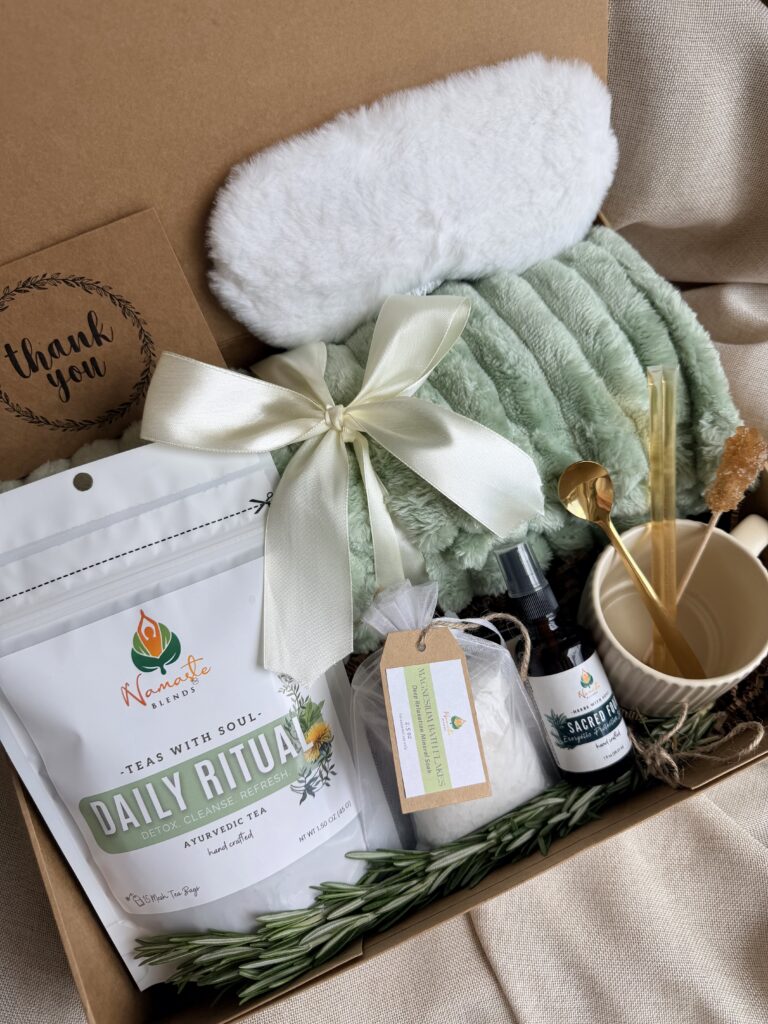 Botanical Reset Gift Box featuring Daily Ritual Herbal Tea, cozy blanket, eye mask, magnesium bath flakes, pillow mist, honey stick, ceramic tea cup, and wellness accessories by Namaste Blends.