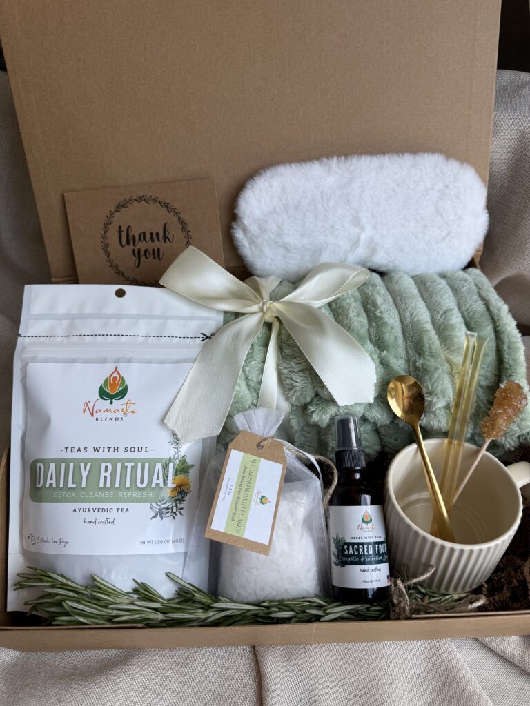 Botanical Reset Gift Box featuring Daily Ritual Herbal Tea, cozy blanket, eye mask, magnesium bath flakes, pillow mist, honey stick, ceramic tea cup, and wellness accessories by Namaste Blends.