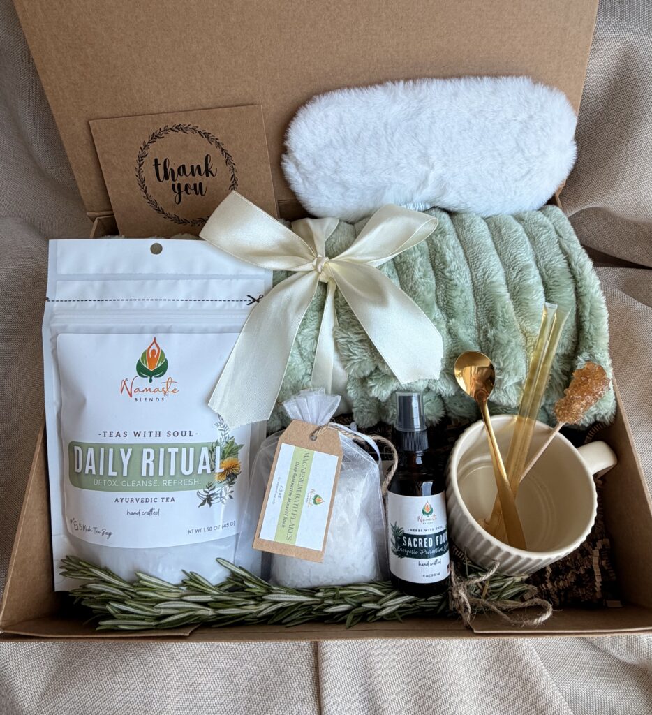 Botanical Reset Gift Box featuring Daily Ritual Herbal Tea, cozy blanket, eye mask, magnesium bath flakes, pillow mist, honey stick, ceramic tea cup, and wellness accessories by Namaste Blends.