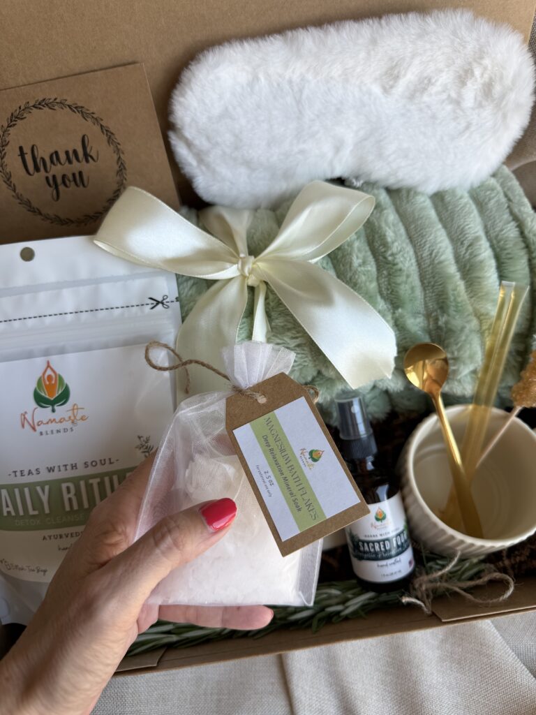Botanical Reset Gift Box featuring Daily Ritual Herbal Tea, cozy blanket, eye mask, magnesium bath flakes, pillow mist, honey stick, ceramic tea cup, and wellness accessories by Namaste Blends.