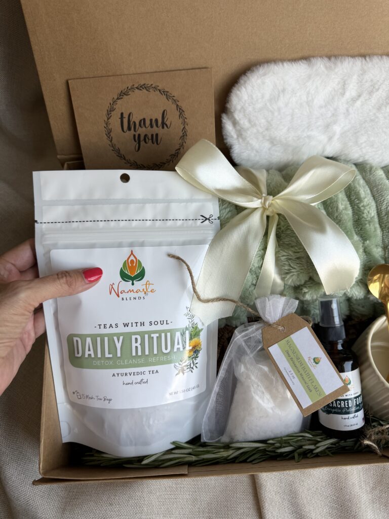Botanical Reset Gift Box featuring Daily Ritual Herbal Tea, cozy blanket, eye mask, magnesium bath flakes, pillow mist, honey stick, ceramic tea cup, and wellness accessories by Namaste Blends.